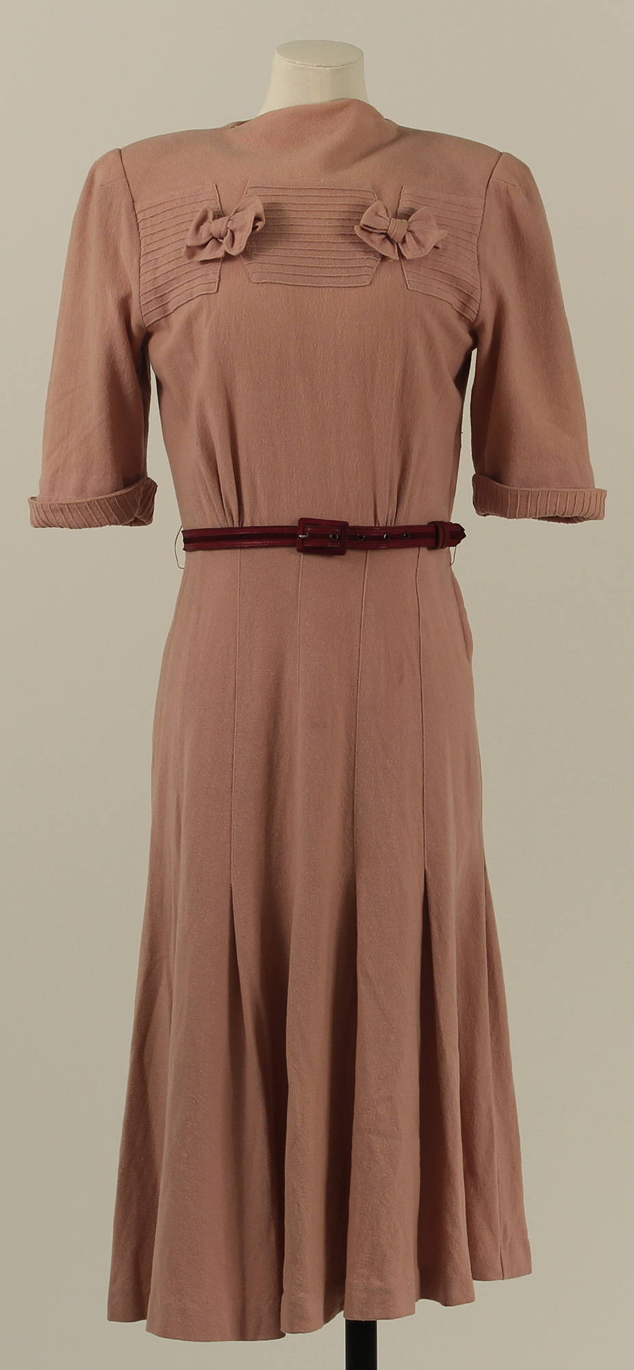A dusty pink dress in typical 1940s style with half-length sleeves, a cinched waist and a pleated skirt falling a little below the knee