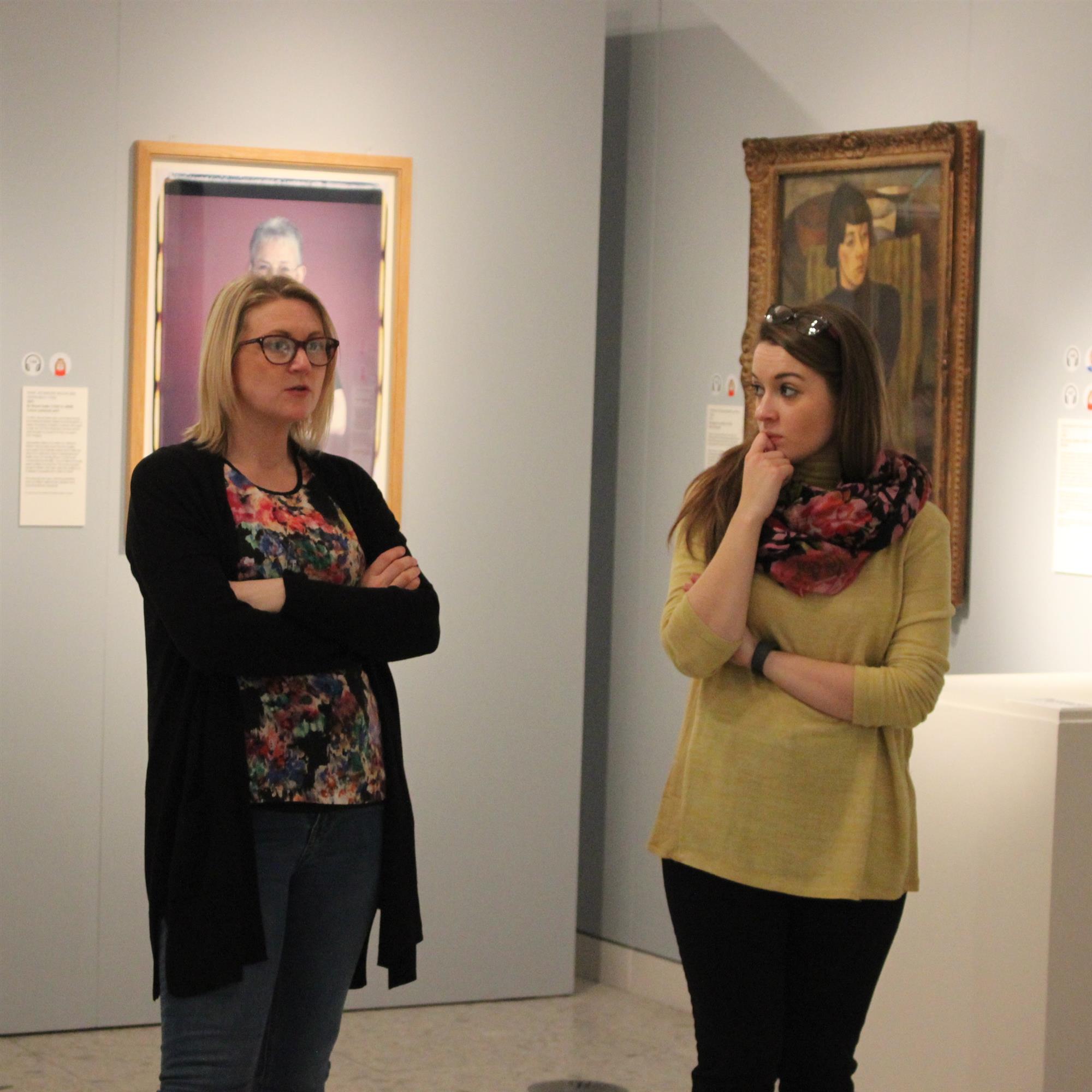Two thoughtful women stand in front of portraits