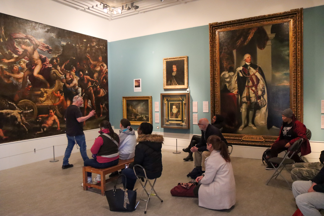 People gathered in the Old Masters gallery at the Herbert Art Gallery & Museum, listening to a member of staff speaking about the paintings on display
